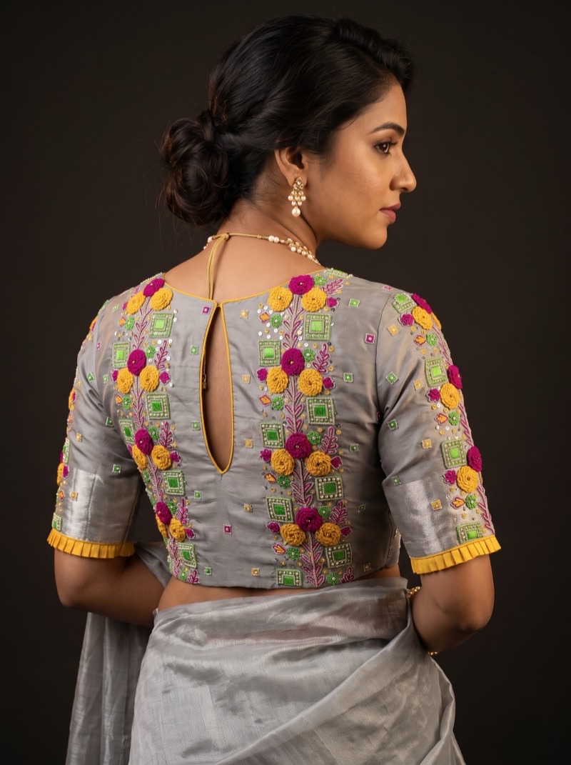Back view of a grey silk blouse with dense aari embroidery in magenta and mustard rosettes and green pearl-outlined squares.
