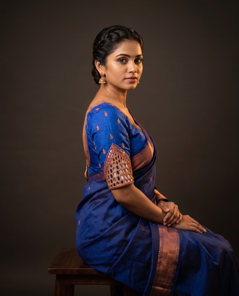 Seated three-quarter front view of a model in the indigo raw silk blouse with copper zari border.