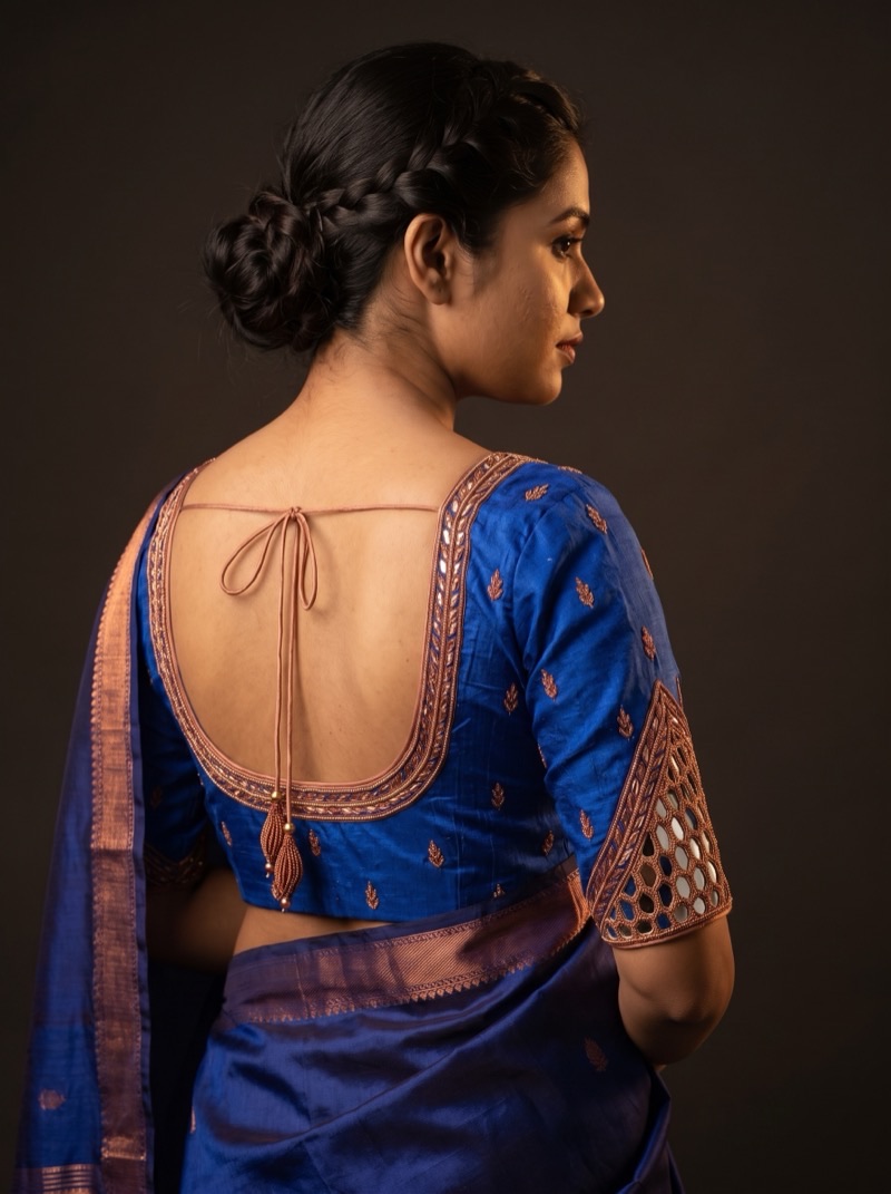 Back view of an indigo raw silk blouse with a copper zari border set with mirrors and a mirror-work lattice sleeve.