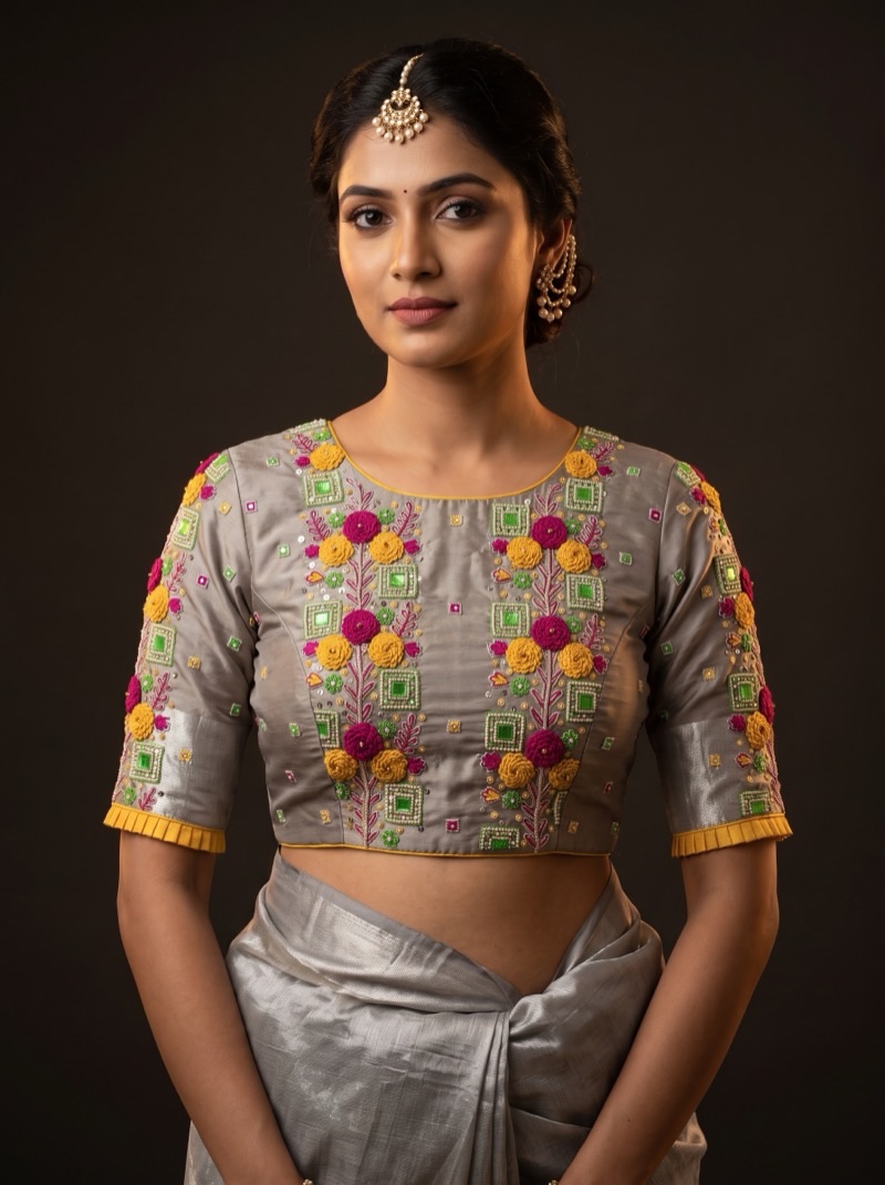 Front view of the grey silk aari blouse with mustard piping at the neckline and a pleated mustard hem.